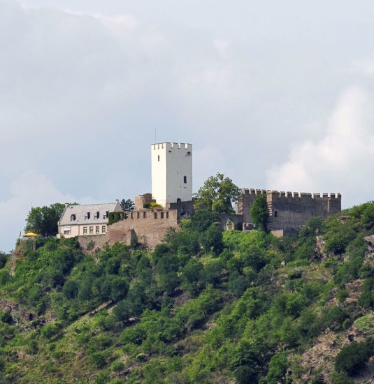 Burg Sterrenberg, geschützt von einer massiven Schutzmauer
Burg Sterrenberg dürfte eine der ältesten Burganlagen am Mittelrhein sein: Ihr Bergfried entstand spätestens Ende des 12. Jahrhunderts. Neben ihrem Alter weist die Burg Sterrenberg jedoch als Besonderheit zwei aufeinanderfolgende Schildmauern auf. Die äußere ist noch stärker und höher als die innere und eindeutig gegen die benachbarte Burg Liebenstein gerichtet. An diesen beiden, einst bitter verfeindeten Burganlagen lässt sich die Jahrhunderte prägende Problematik wechselnder Besitzverhältnisse im Mittelrheintal ablesen. Denn im Mittelalter lagen dort oftmals verschiedener Herrscher Territorien direkt nebeneinander. Mancherlei Feindseligkeit der Fürsten, Grafen oder Äbte manifestierte sich in den, die Herrschaftsgebiete absichernden, Gegenburgen. | © Romantischer Rhein Tourismus GmbH