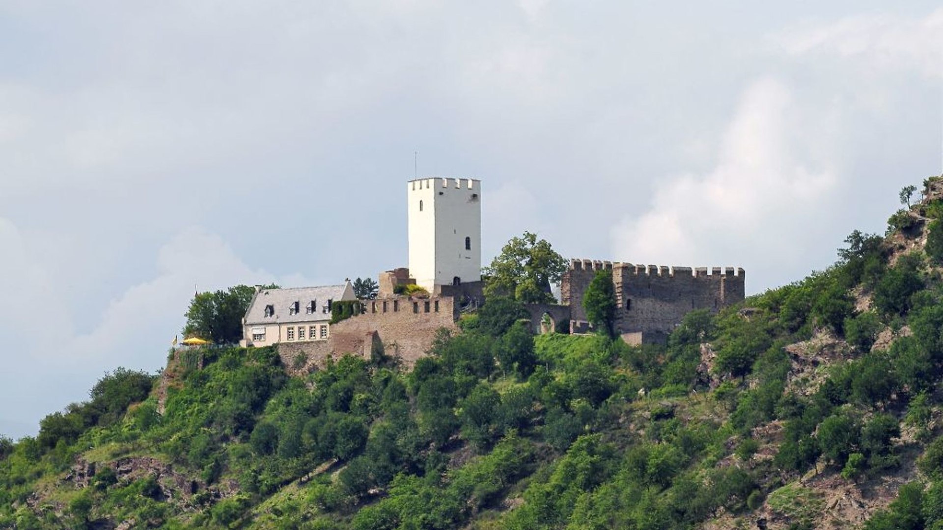 Burg Sterrenberg, geschützt von einer massiven Schutzmauer
Burg Sterrenberg dürfte eine der ältesten Burganlagen am Mittelrhein sein: Ihr Bergfried entstand spätestens Ende des 12. Jahrhunderts. Neben ihrem Alter weist die Burg Sterrenberg jedoch als Besonderheit zwei aufeinanderfolgende Schildmauern auf. Die äußere ist noch stärker und höher als die innere und eindeutig gegen die benachbarte Burg Liebenstein gerichtet. An diesen beiden, einst bitter verfeindeten Burganlagen lässt sich die Jahrhunderte prägende Problematik wechselnder Besitzverhältnisse im Mittelrheintal ablesen. Denn im Mittelalter lagen dort oftmals verschiedener Herrscher Territorien direkt nebeneinander. Mancherlei Feindseligkeit der Fürsten, Grafen oder Äbte manifestierte sich in den, die Herrschaftsgebiete absichernden, Gegenburgen. | © Romantischer Rhein Tourismus GmbH